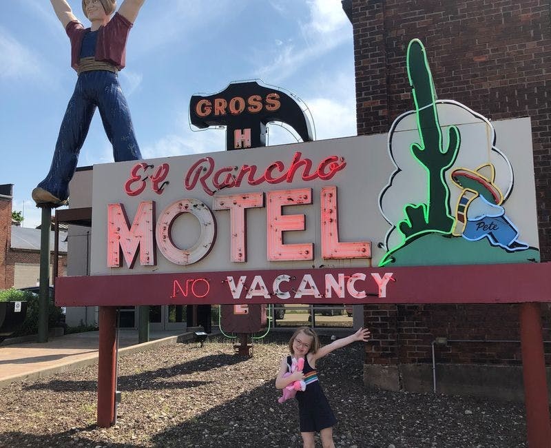 a small female child in front of a neon sign for el rancho motel