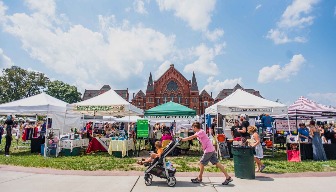 boy pushes his younger sibling in a stroller on sideway in front of city flea market