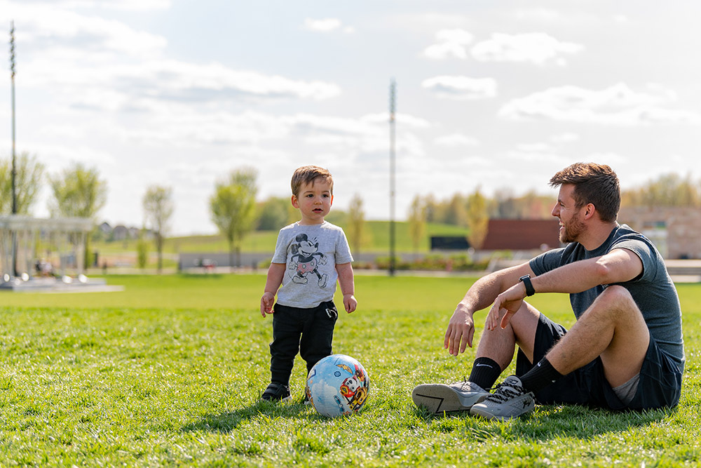 Son and dad playing with a soccer ball at the park